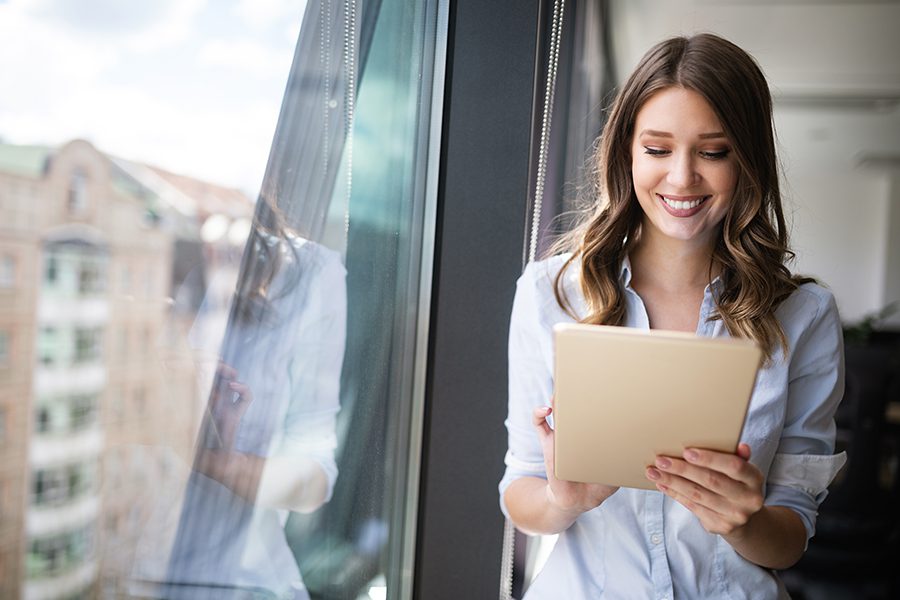 客户中心-快乐的女人拿着平板电脑，站在她的现代办公室
