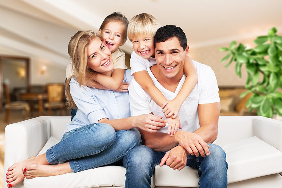 Personal Insurance - Portrait of a Young Family at Home Smiling and Sitting on the Sofa in Their Living Room